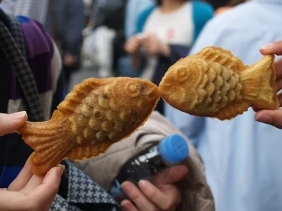 Twee mensen houden taiyaki's omhoog, zodat het lijkt alsof de visjes zoenen