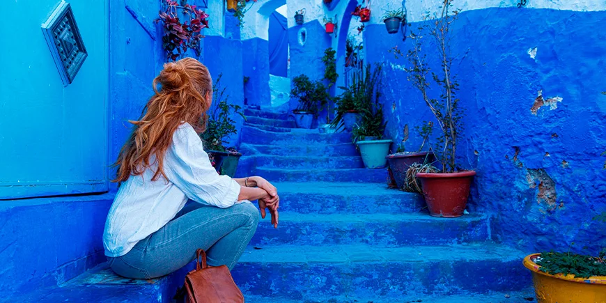Vrouw zit op trap in de blauwe stad Chefchaouen in Marokko