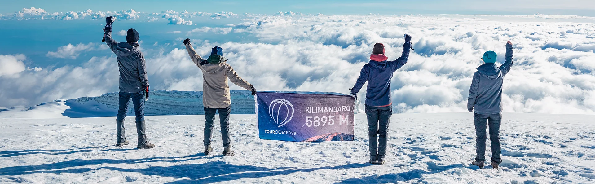 Groep met een TourCompass-spandoek op de top van de Kilimanjaro